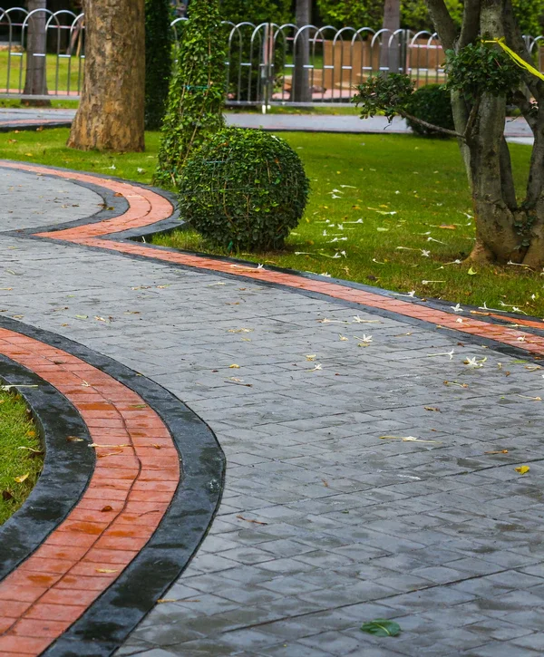 A curved outdoor walkway featuring two-toned decorative concrete staining in Powell, TN, with a grey textured center and reddish-brown borders surrounded by green grass.