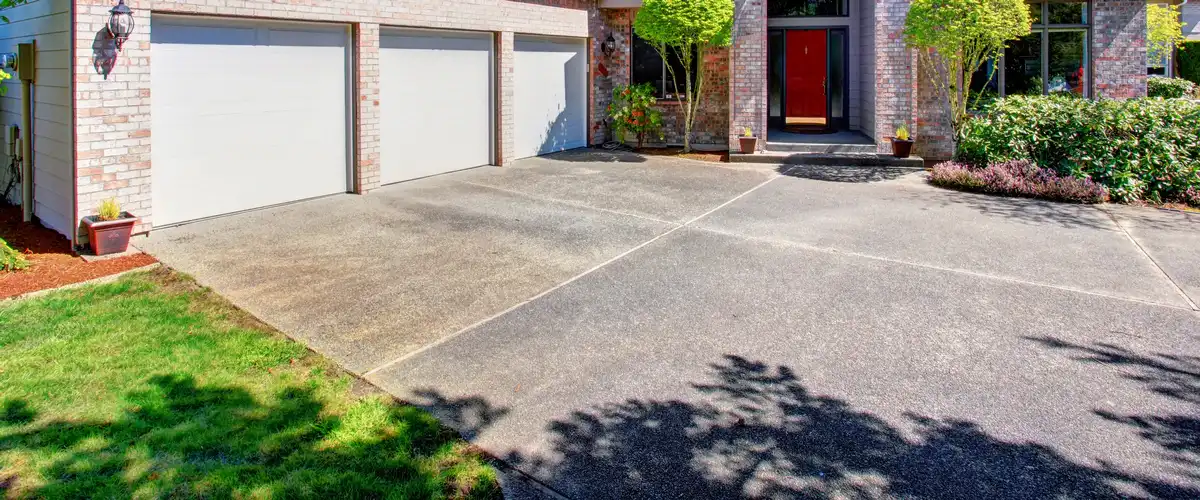 A wide residential concrete driveway leading to a three-car garage and red front door, showcasing an established concrete resurfacing application.