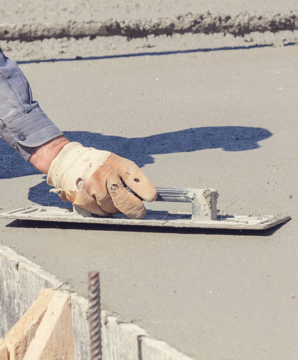 Close-up of a worker wearing a protective glove using a hand trowel for concrete leveling on a fresh pour next to rebar in Powell, TN.