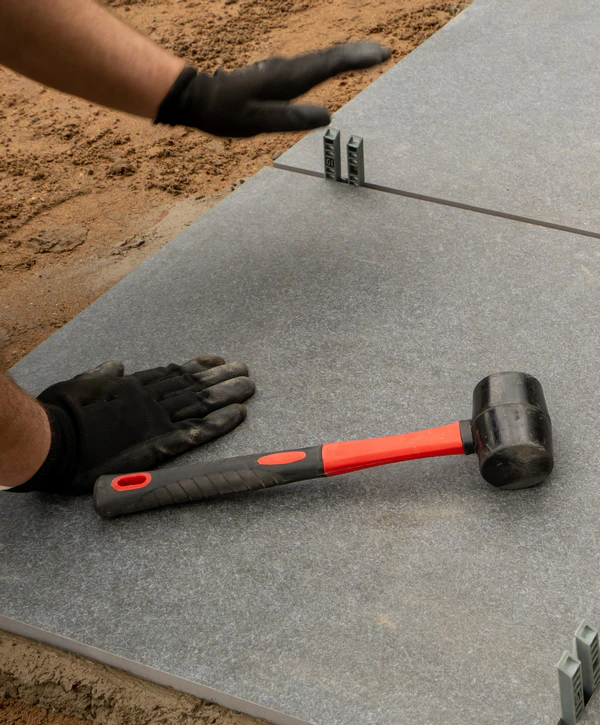 Gloved hands using a red and black rubber mallet to align and install large precast concrete slab pavers with leveling spacers in Powell, TN.