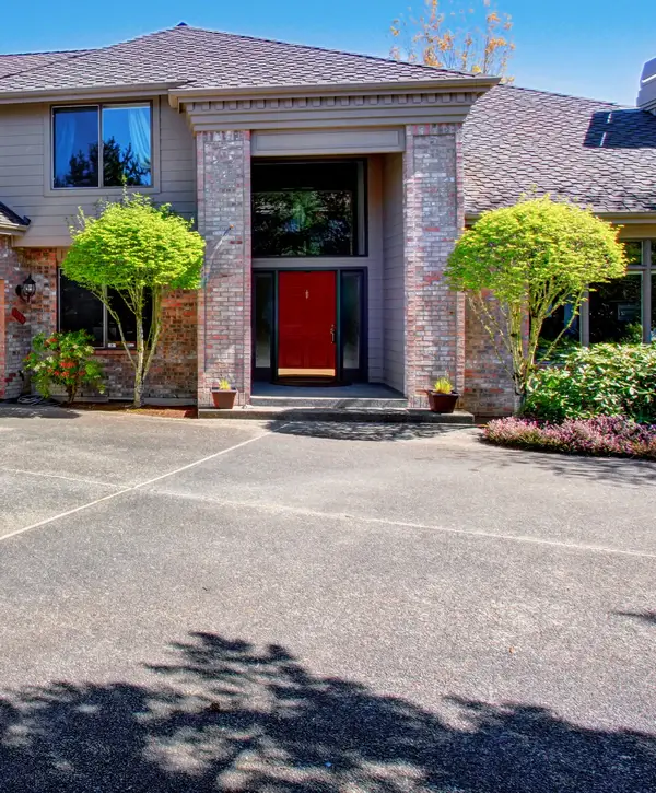 A wide concrete driveway leading up to a large house with a bright red front door and brick accents, showcasing seamless concrete patching in Powell, TN.